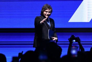 Javier Milei en un acto público, bajo luces azules, con carpeta en mano